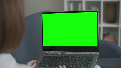 mujer en casa sentada en un sofá trabaja en una computadora portátil con pantalla de maqueta verde. educación remota de cuarentena de coronavirus covid-19 o concepto de trabajo. niña usando computadora, navegando a través