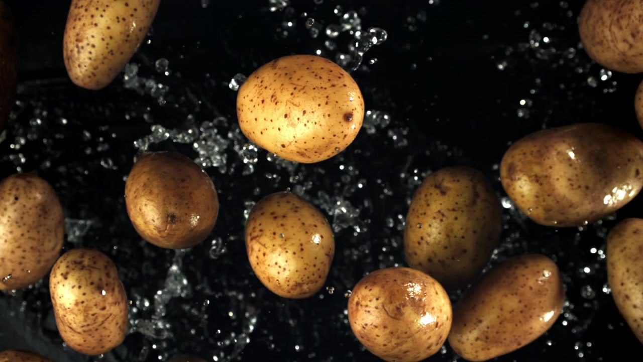 Rallentatore di patate fresche che cadono con schizzi d'acqua su sfondo nero.