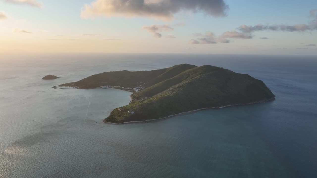 Sanfter Drohnenflug über Hayman Island zur goldenen Stunde, der die üppige Kammlinie und die geschützte Bucht, umgeben von ruhigem blauem Ozean, in den Whitsundays, Queensland, Australien, zeigt.