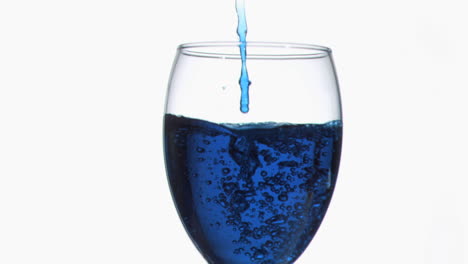 un fino goteo azul en súper cámara lenta fluyendo en un vaso de vino lleno