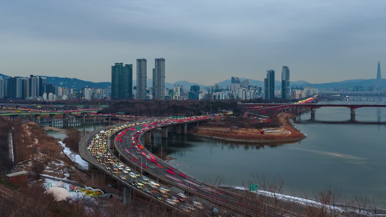 Seul, Corea del Sud - hyperlapse, traffico intenso sull'autostrada Gangbyeonbuk-ro, strada sopraelevata curva, Ponte Seongsu, Fiume Han, skyline con Lotte Tower, montagne, transizione giorno-ora blu inverno
