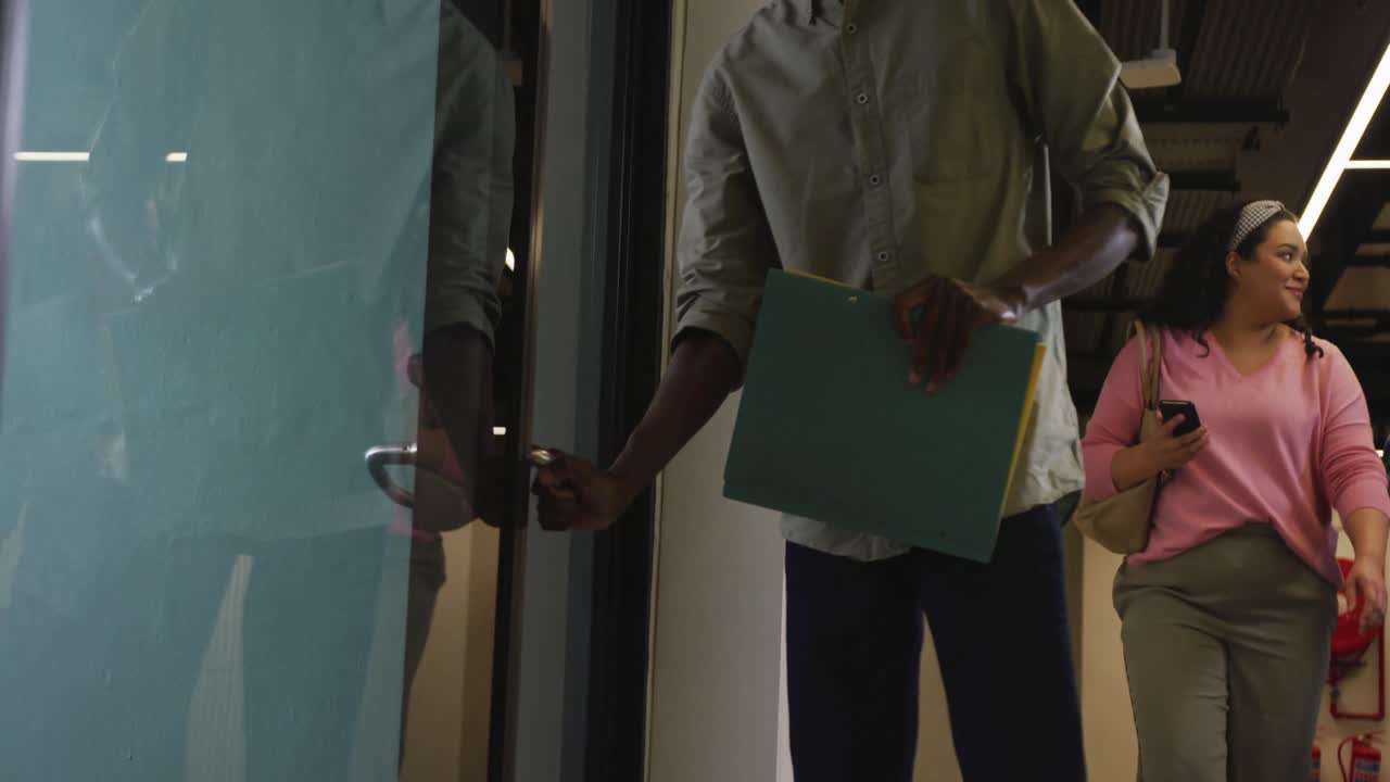 Felici professionisti di diverse etnie che camminano con documenti e aprono una porta in ufficio.