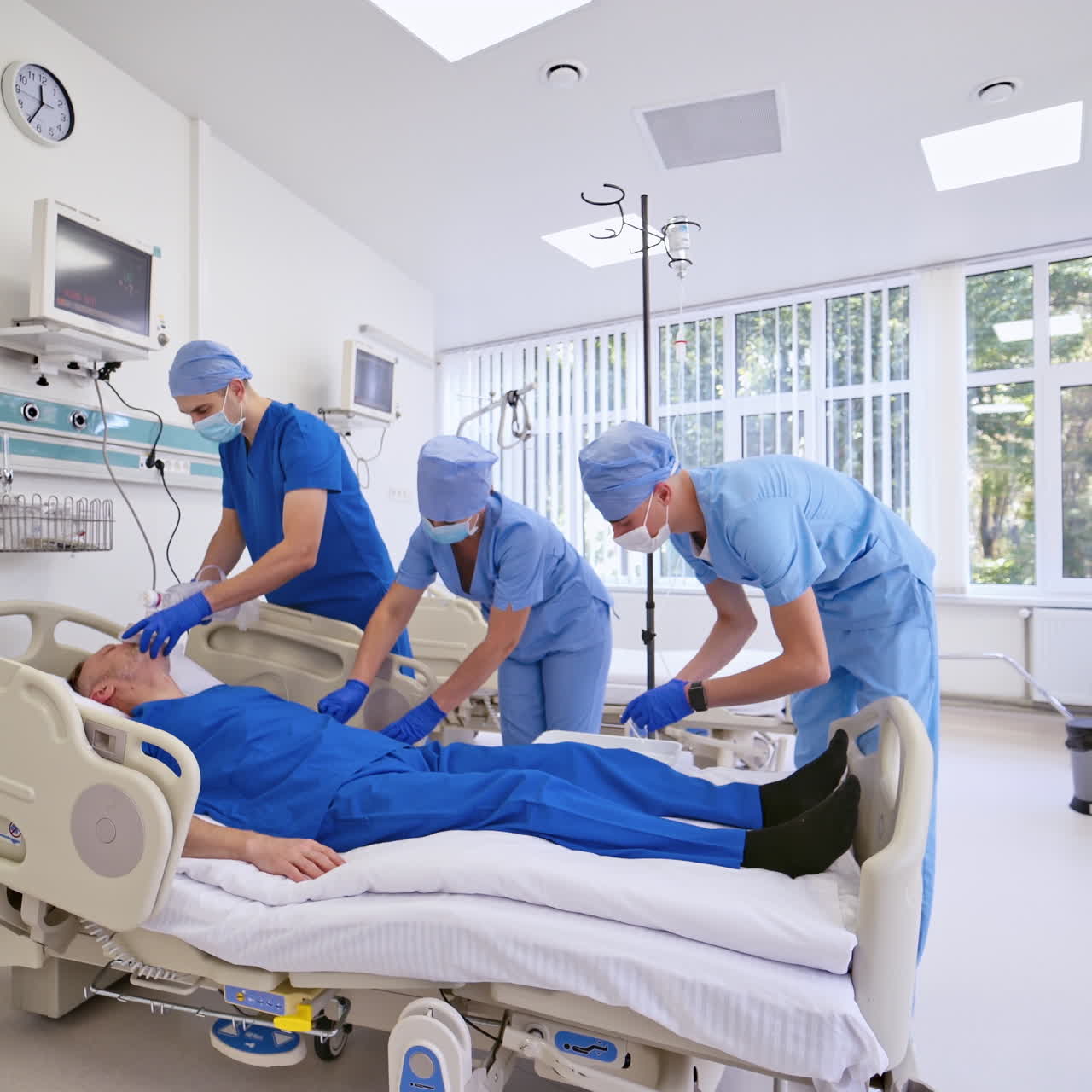 Teamwork of doctors with patient in the emergency room. Man patient is lying on bed in modern clinic and medical staff giving a resusculation.