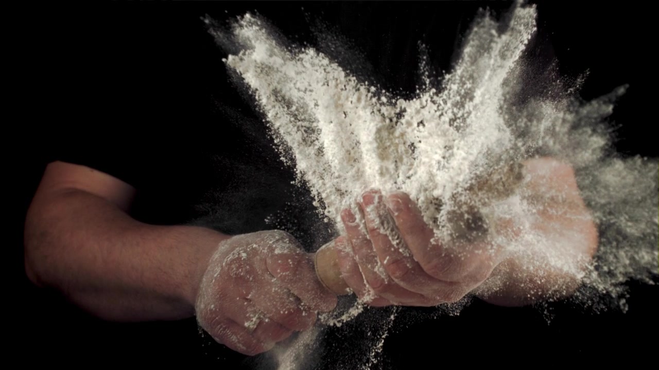 Slowmotion mel-eksplosion fra hænder med kagerulle på sort baggrund