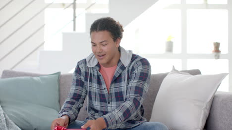 Happy-biracial-man-having-video-call-and-holding-present-in-sunny-living-room,-slow-motion