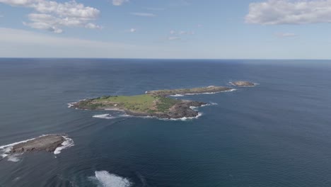 aerial dolly to remote low tropical rocky island with grassy patch and shrubs off coast of port kembla nsw australia