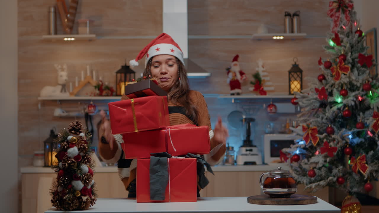 mujer con sombrero de santa llevando regalos en la cocina decorada