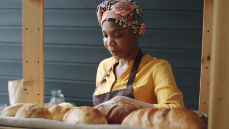 cheerful black woman putting fresh bread on shelve in bakery