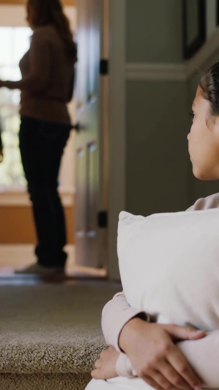 Vídeo vertical: Observando uma adolescente abraçando um travesseiro na escada de casa, um dos pais na porta com chaves