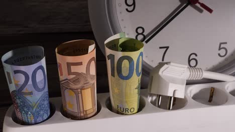 closeup shot of money on an electrical socket with a clock behind them.