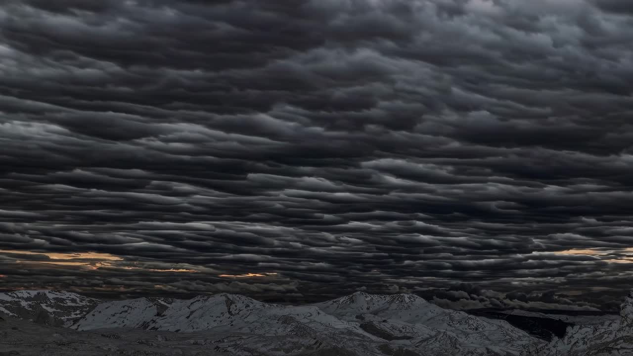The video captures dramatic, swirling storm clouds over rugged mountains, creating a moody