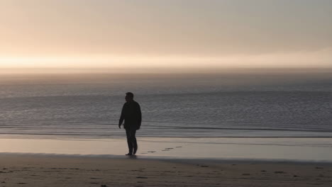 solitary figure walking on a misty beach at sunset