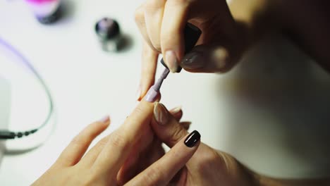 master of manicure is covering nails by gel varnish in pastel-colored on the table in the beauty salon