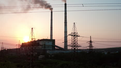 panoramic view on harmful power station at sunset. tall electricity pylons next to large factory with smoke stacks on the evening sky. camera rising up.