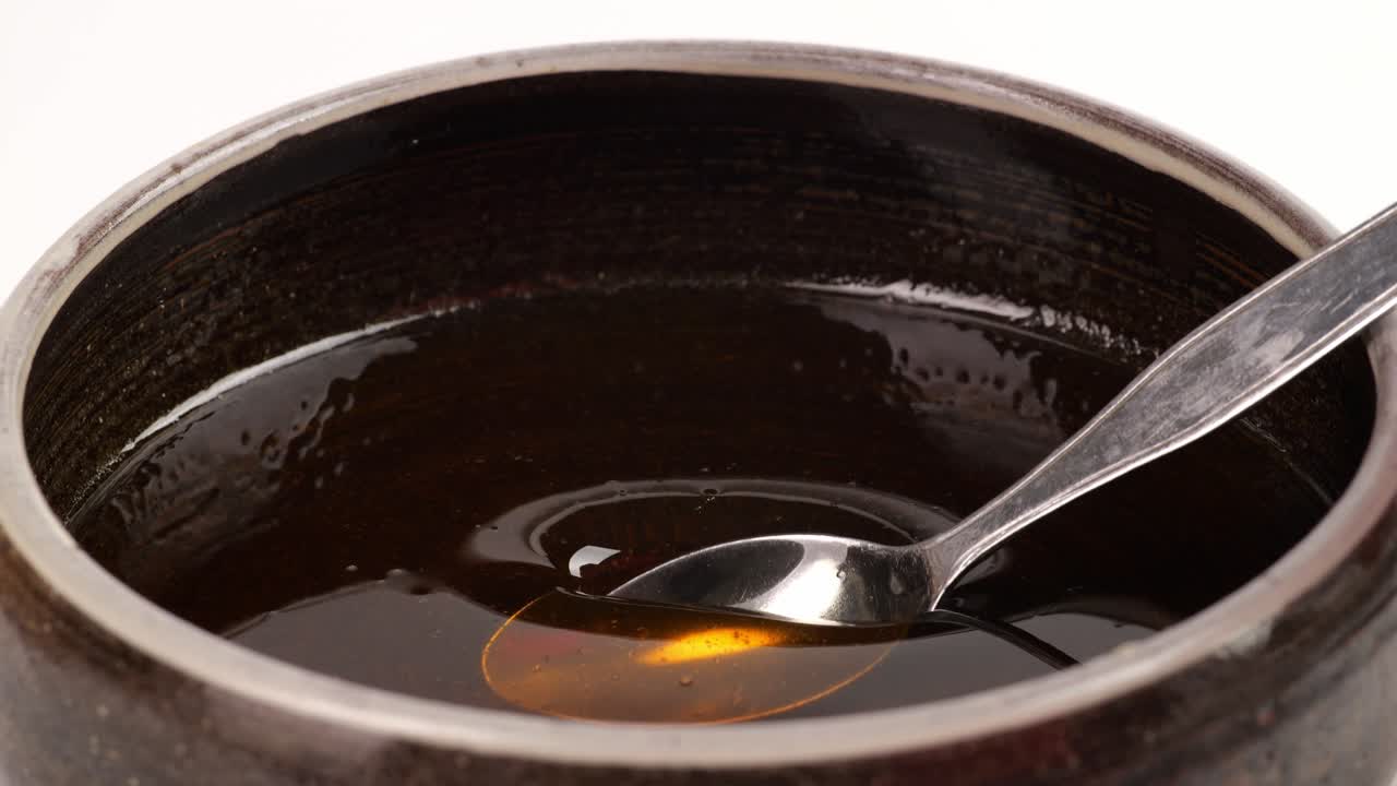 una cuchara de metal se sumerge para tomar miel en un cuenco sobre el fondo blanco. miel goteando de la cuchara de metall, saludable orgánica miel gruesa de primer plano, dulce postre de miel 4k. cámara lenta