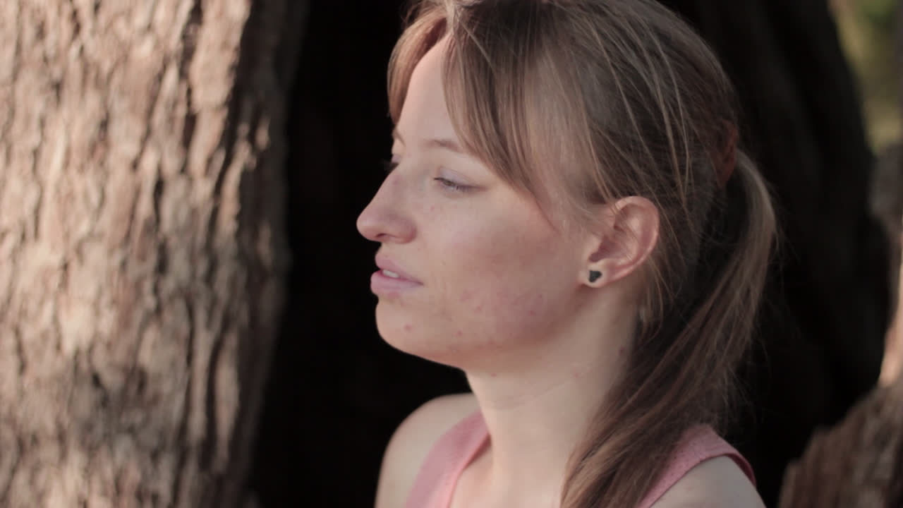 primer plano de una mujer joven sentada debajo del árbol y respira profundamente para relajarse