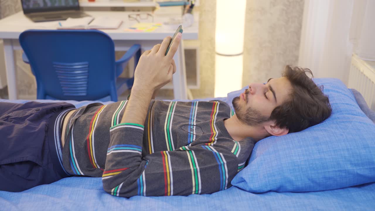 un joven somnoliento mirando el teléfono en la cama.
