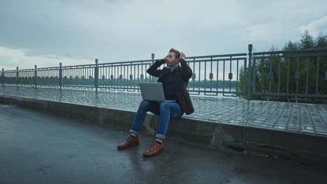 man stressed outdoor working on laptop in the rain
