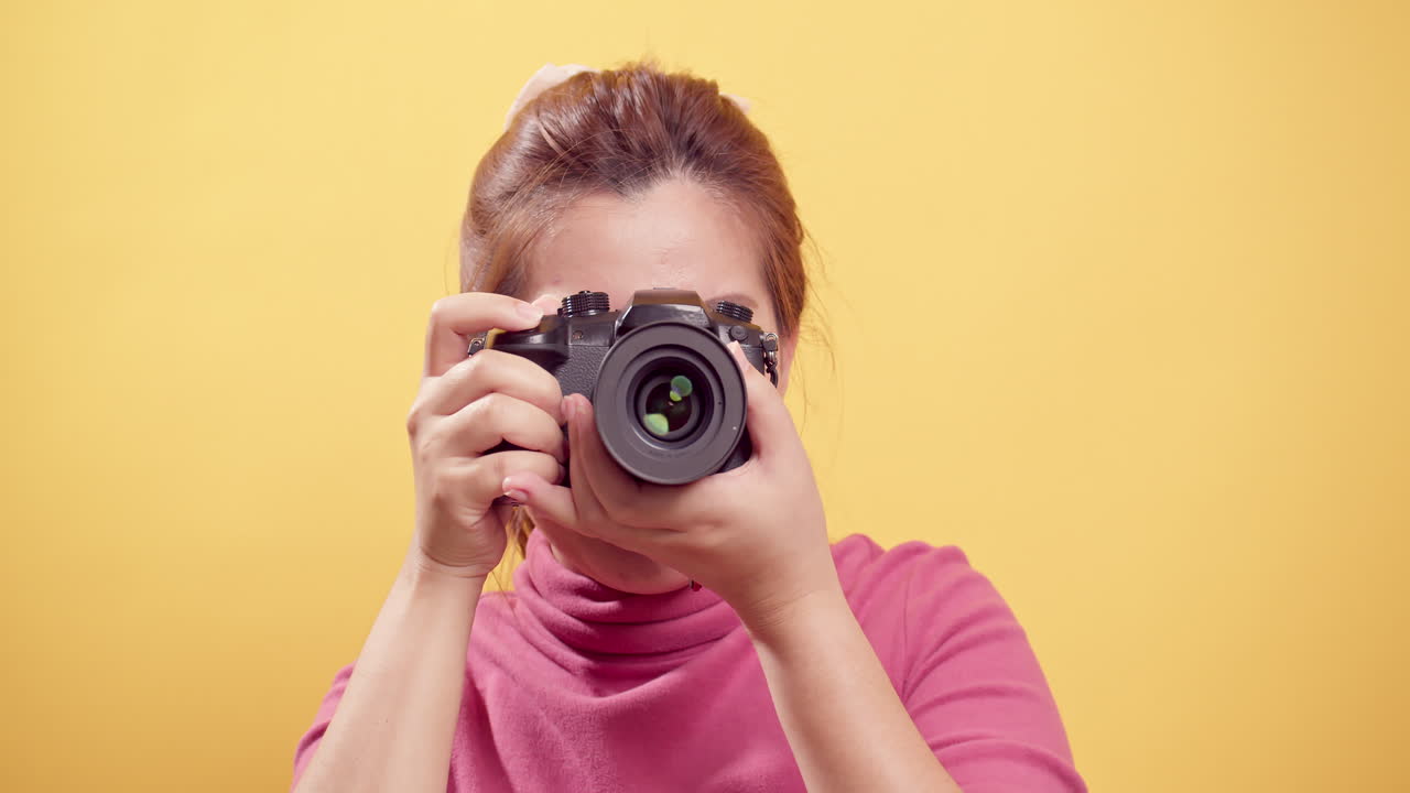 Brunette young Asian woman happy and joyous, smiling proudly with a digital camera and isolated yellow background