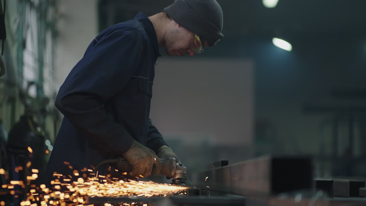 Un uomo con occhiali protettivi lavora alla molatura, lucidatura e sverniciatura di strutture metalliche in acciaio. Slow motion.
