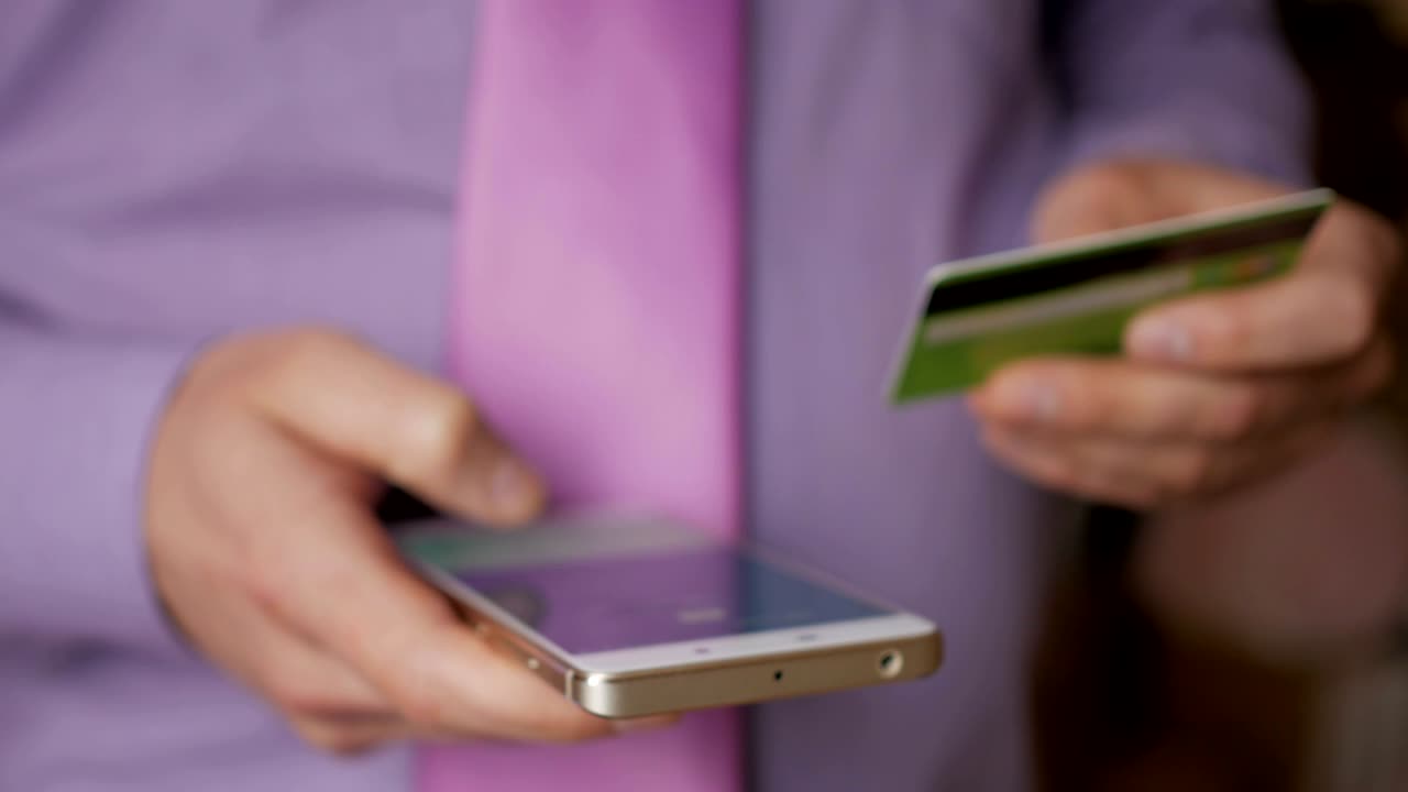 hombre de negocios con una camisa púrpura haciendo pago en línea con tarjeta de crédito y teléfono inteligente, compras en línea, tecnología de estilo de vida. hombre introduce el número de tarjeta bancaria en el teléfono inteligente. primer plano. primer plano
