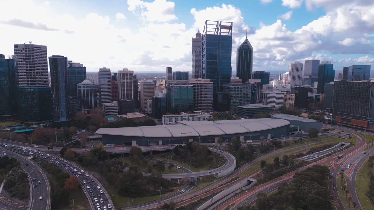 Aerial footage of the Perth CBD Skyline, with heavy traffic on the Mitchell Freeway on a bright, cloudy afternoon in Perth, Western Australia