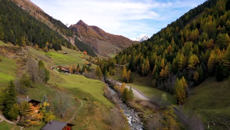 drone flying above swiss village in autumn : fall with mountains and a river on the background