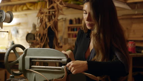 diseñadora de calzado femenina cortando la suela de la bota trabajando en una máquina antigua en el taller