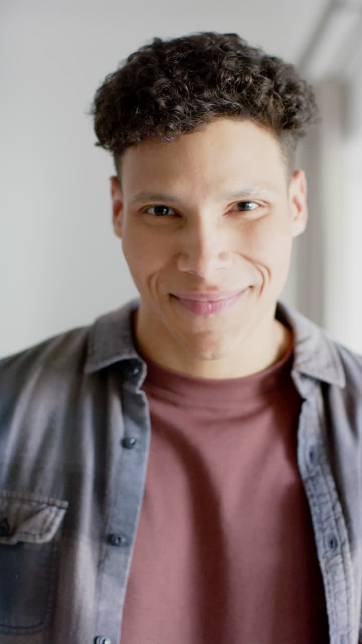 Vertical video of portrait of happy biracial man at home, in slow motion