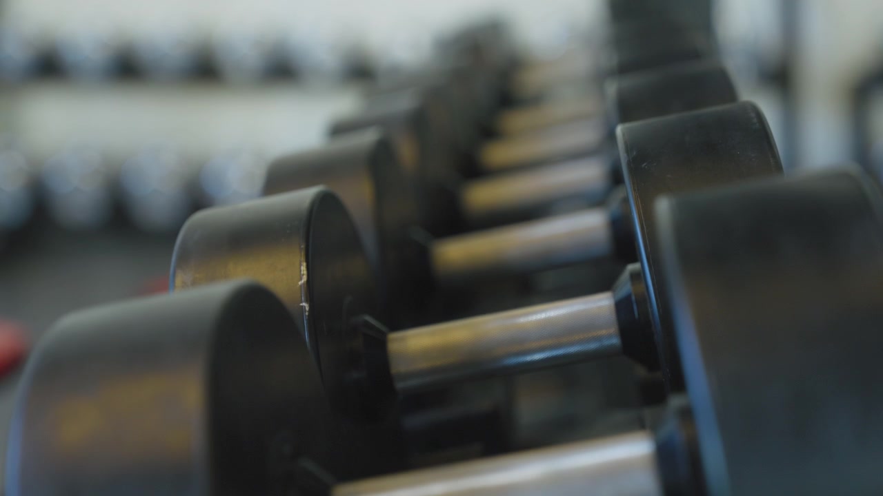 Rack focus down a line of rubber dumbbells on a rack in an indoor gym