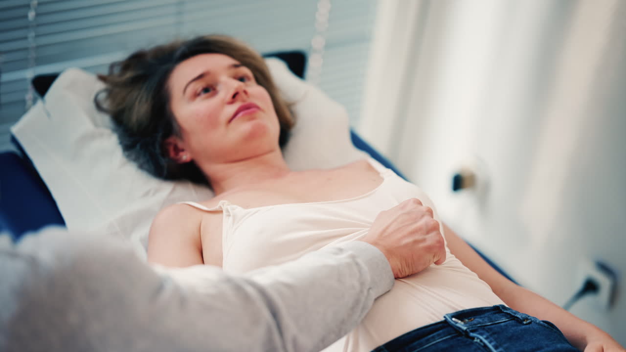 Un terapeuta esamina una donna distesa su un lettino medico, posizionando le mani sull'addome come parte di una valutazione o di un trattamento