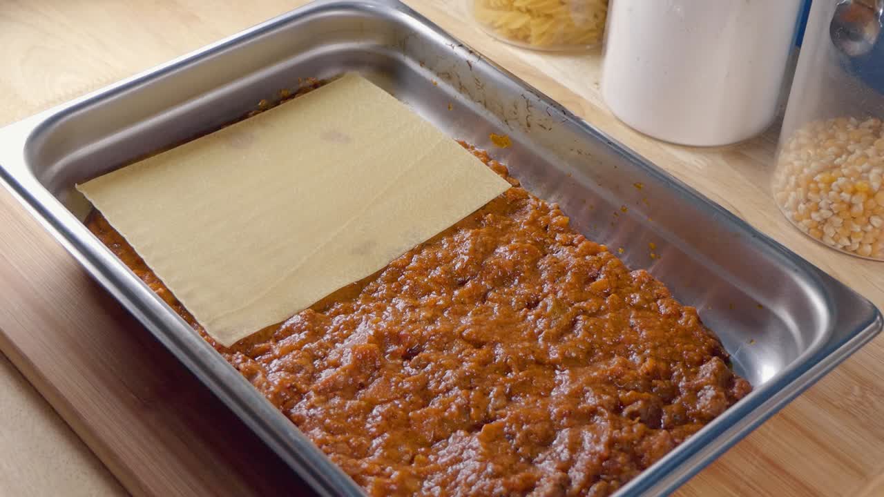 plano medio de agregar láminas de pasta a la salsa de tomate en una bandeja para hornear para hacer lasaña