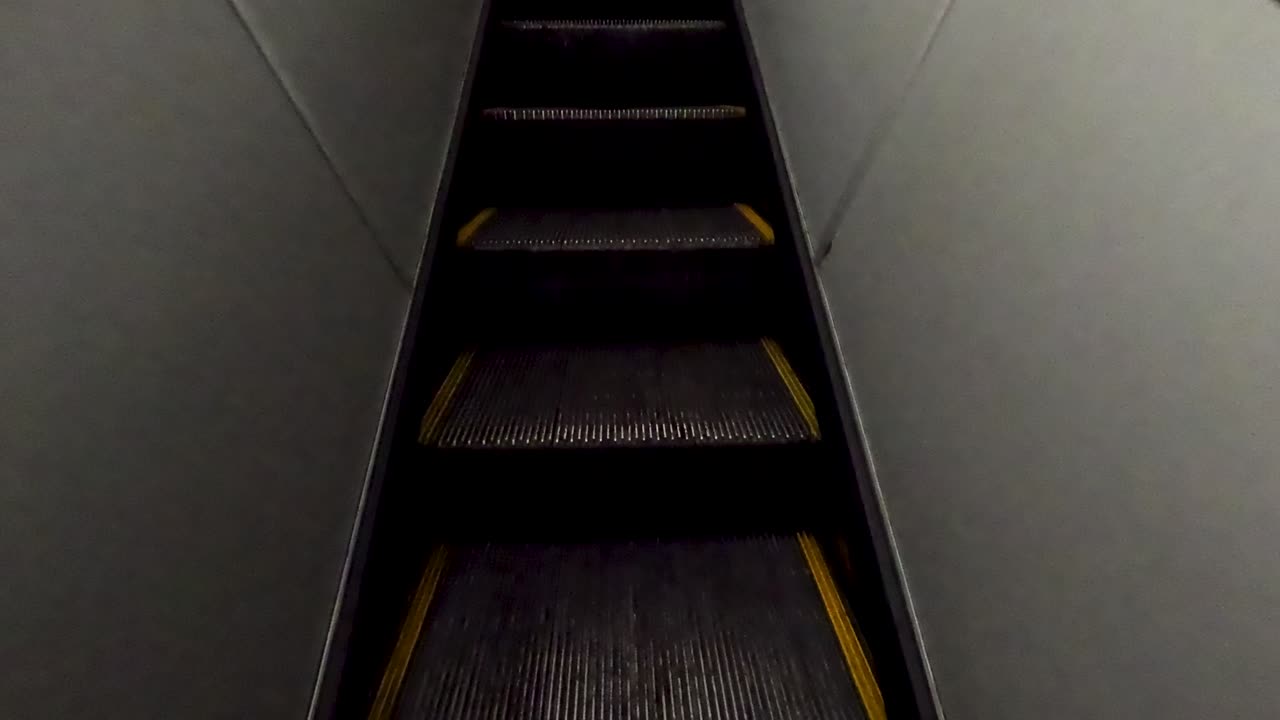 Person walks up the stairs inside an airplane at an airport. Bright lights shine down as they move forward. The interior is simple and clean, showing signs of recent use