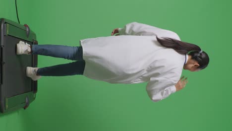 스테토스코프를 들고 있는 아시아 여성 의사가 병원에서 녹색 스크린 배경에서 는 동안 손을 흔들고 미소 짓고 있습니다.