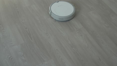 aspiradora robótica blanca en piso laminado limpiando el polvo en el interior de la sala de estar. tecnología de limpieza inteligente.