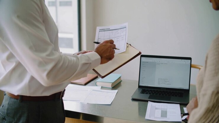 Offering man in white shirt handing document to woman in light sweater at office, marking clipboard