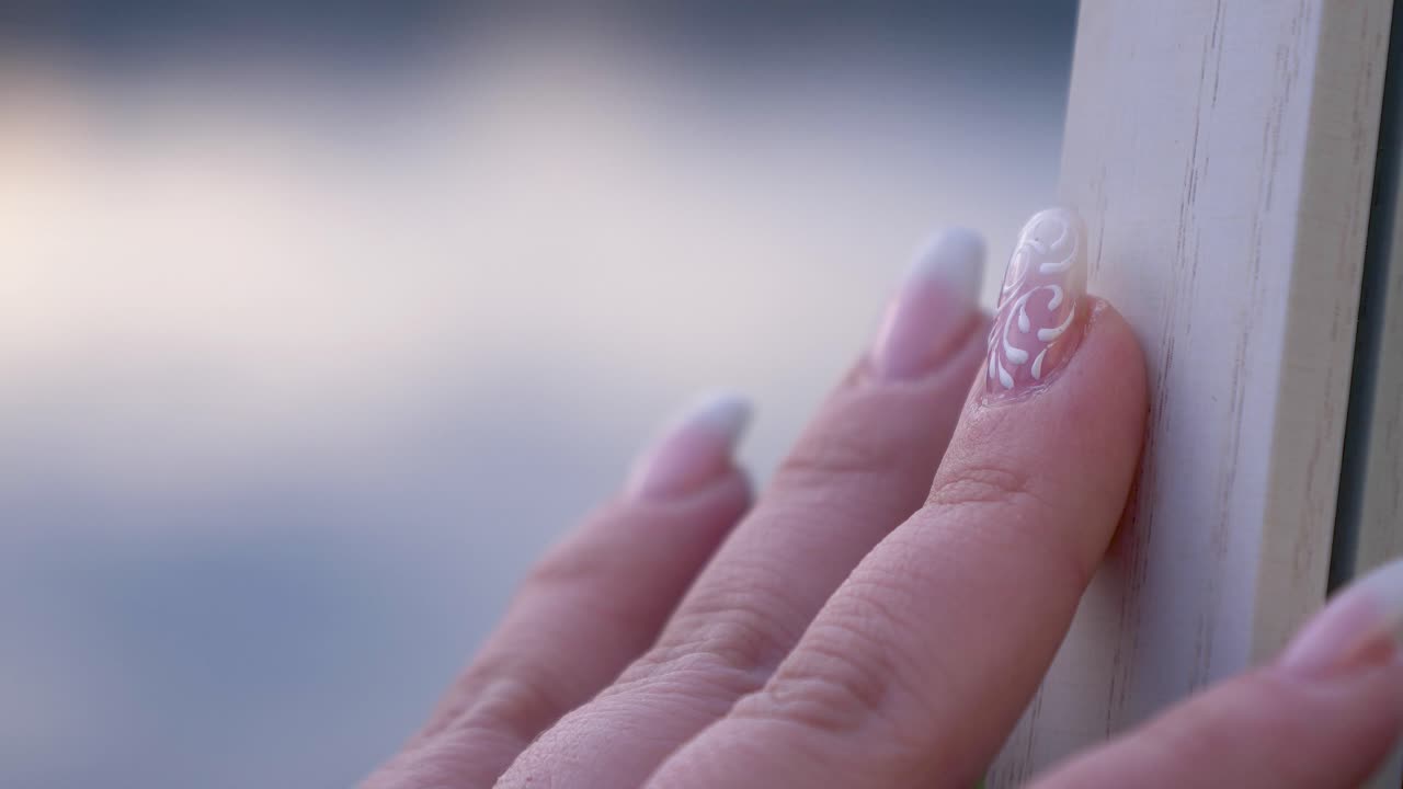 Slow motion close up of white nail art decoration on girl's hand with fingers touching a wood surface