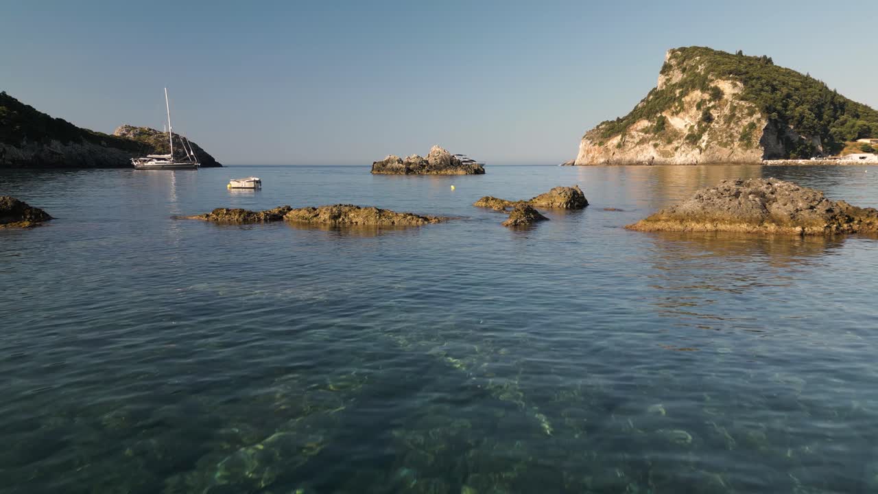 baja dolly aérea se eleva por encima de las rocas sobresalientes y la luz reluciente bajo el agua a la lancha de velocidad yate anclado en el borde de la bahía en corfú grecia