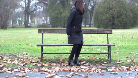 Mujer-Joven-Caminando-En-Un-Parque-Y-Sentada-Sola-En-Un-Banco-En-Un-Día-Frío