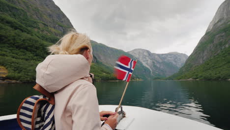 una persona con una bandera noruega en la mano viaja en un barco en un fiordo pintoresco