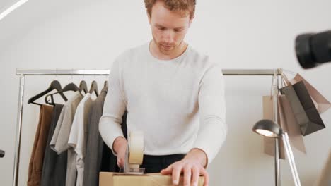 cute curly young man folds a cardboard box with a tape gun