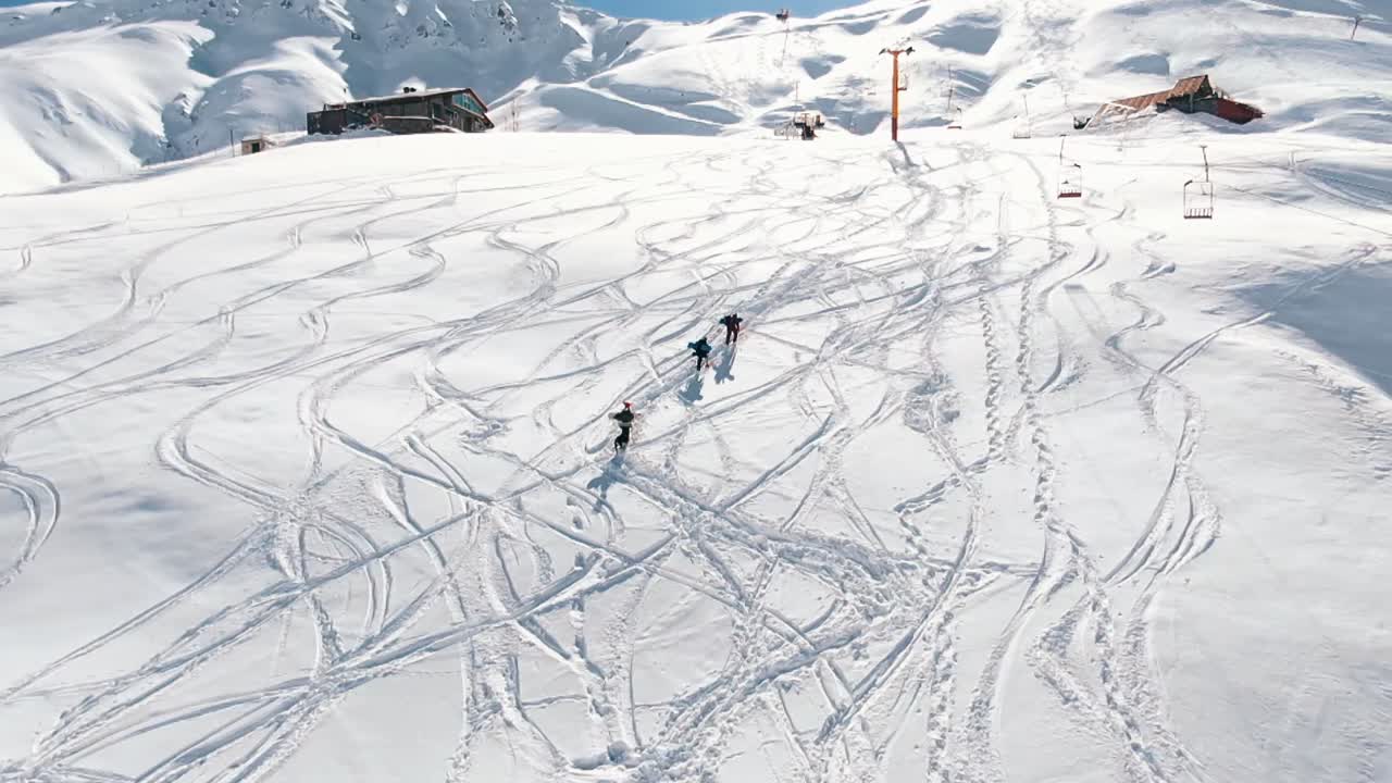 Slow motion: Snow boarders walking up the mountain. Camera moving slowly behind group of snowboarder walking up the mountain