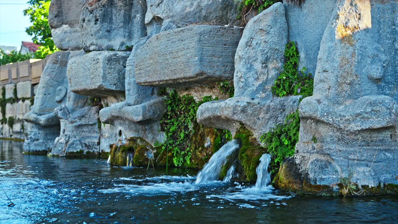 The intricate stone carvings of an ancient water sanctuary, where clear streams flow gently from the mouths of sacred figures. 8k