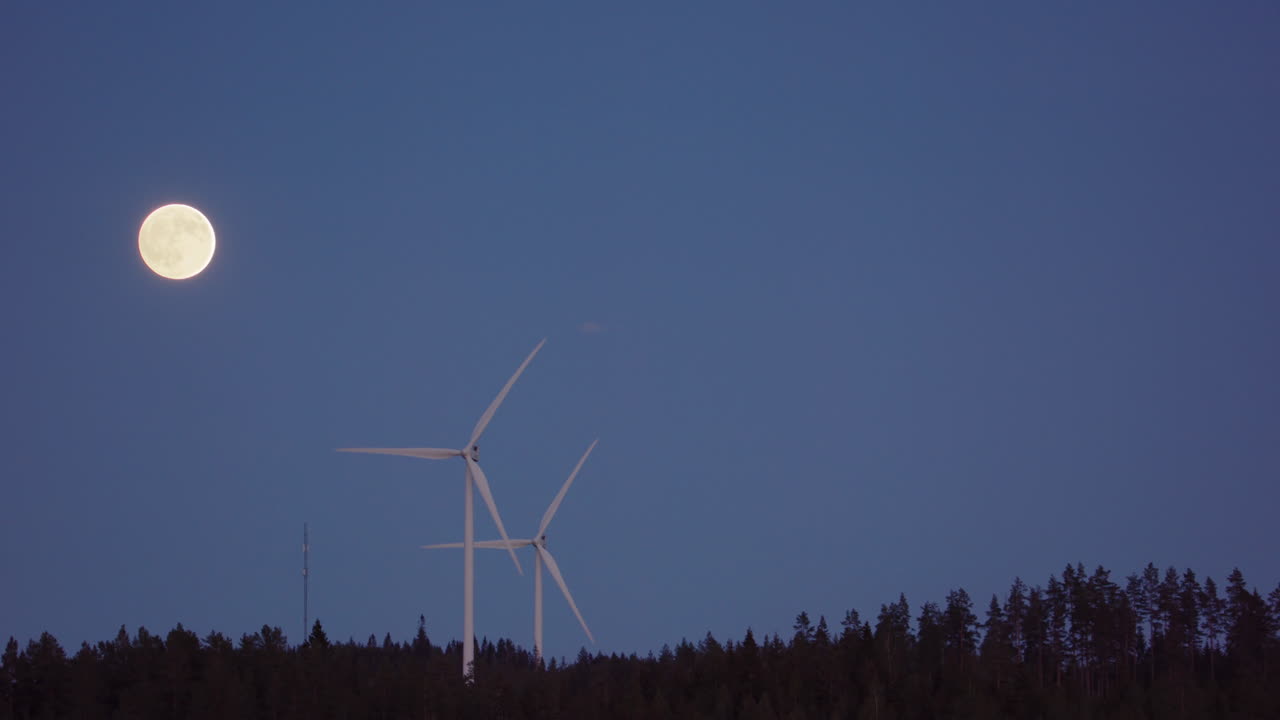 WIDE, SLOW MOTION, ZOOM OUT - Turbines spin next to a rising full moon