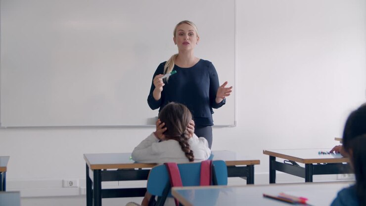 Primary school teacher writing on empty white board