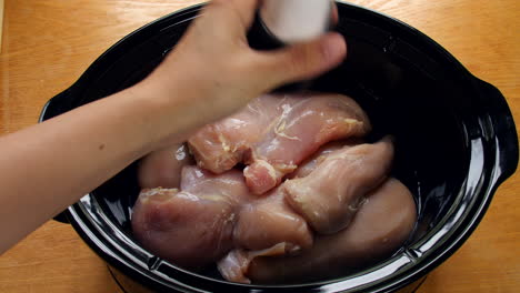 raw chicken is added to a slow cooker and seasoned