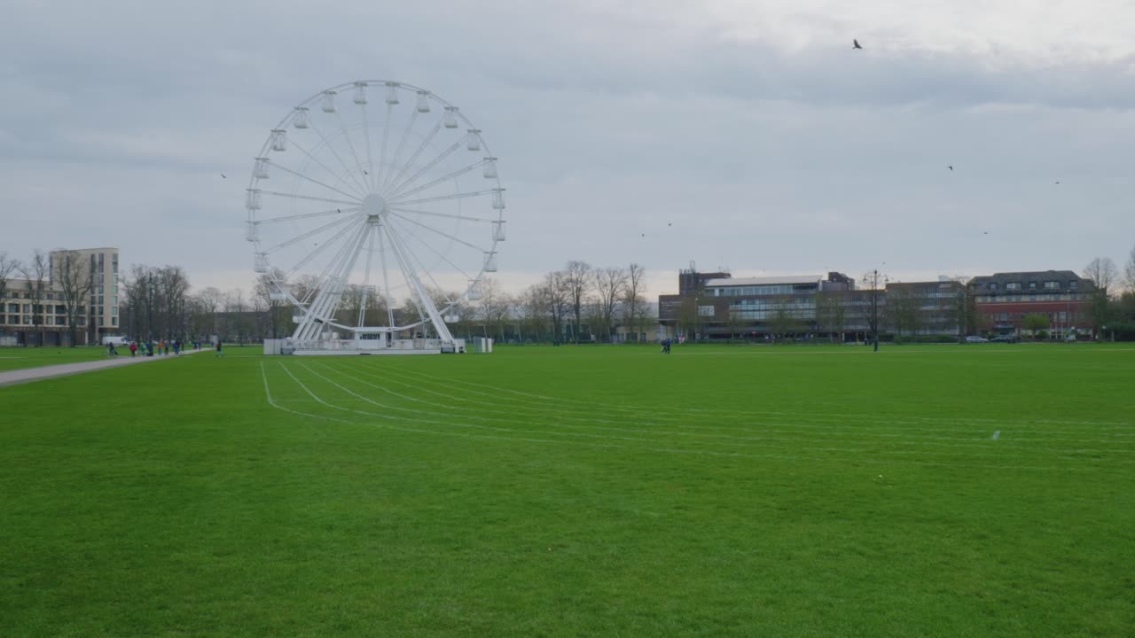 pan a través de la rueda de la fortuna blanca detrás de la pista de hierba verde en cambridge, inglaterra