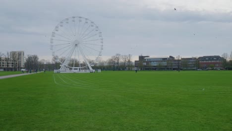 pan across white ferris wheel behind green grass track in cambridge england