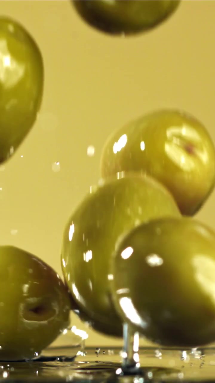 Olive verdi fresche che schizzano al rallentatore su sfondo giallo
