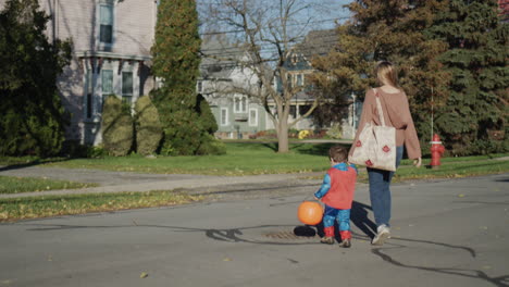 a woman leads by the hand a little boy in a costume, they go for candy on halloween